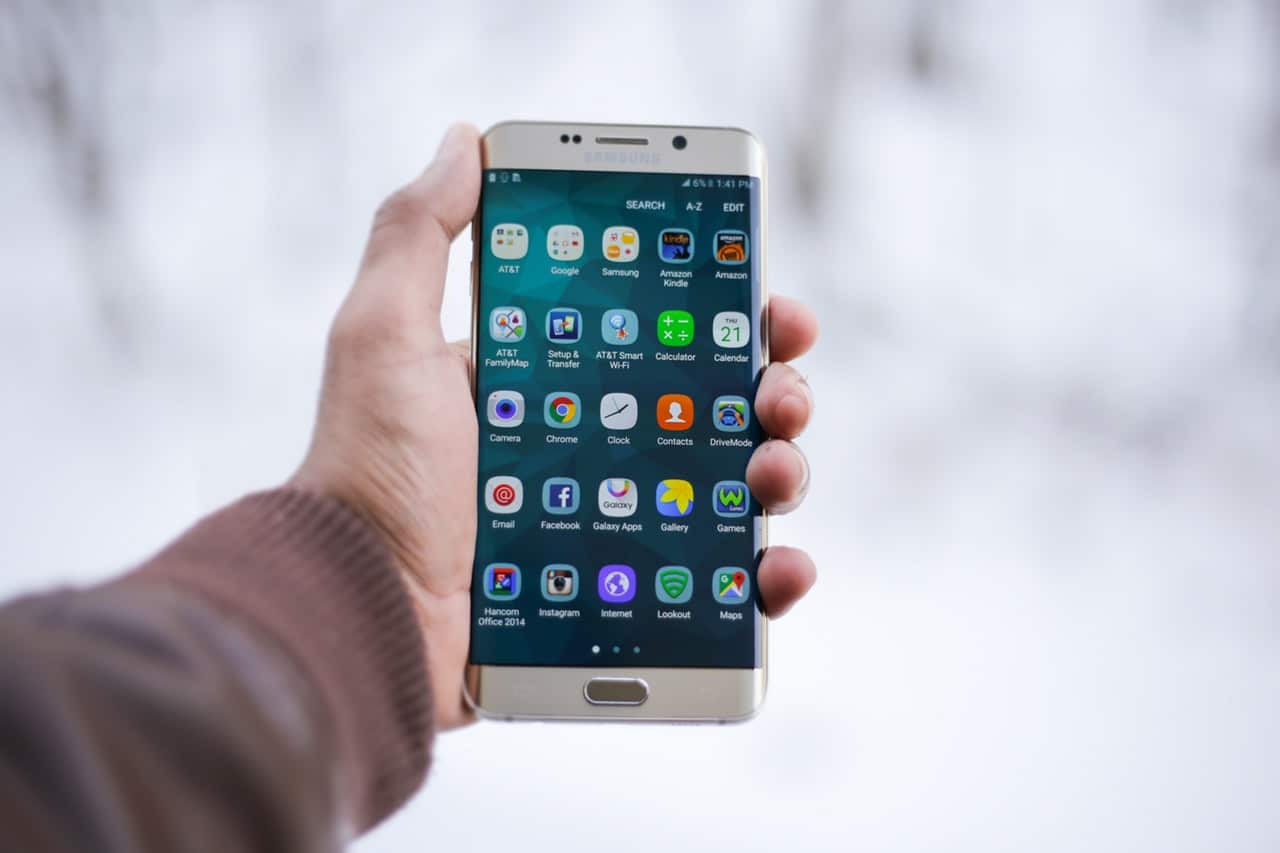 A hand holding a smartphone displaying a variety of apps