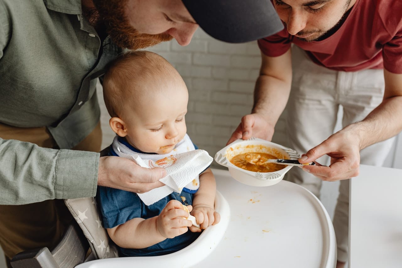 Two fathers feeding their baby