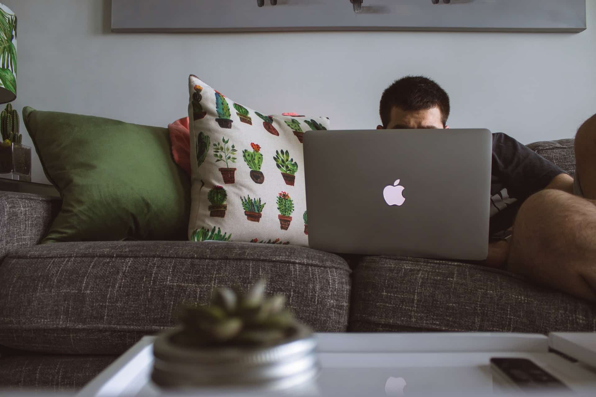 man using macbook sitting on sofa bed