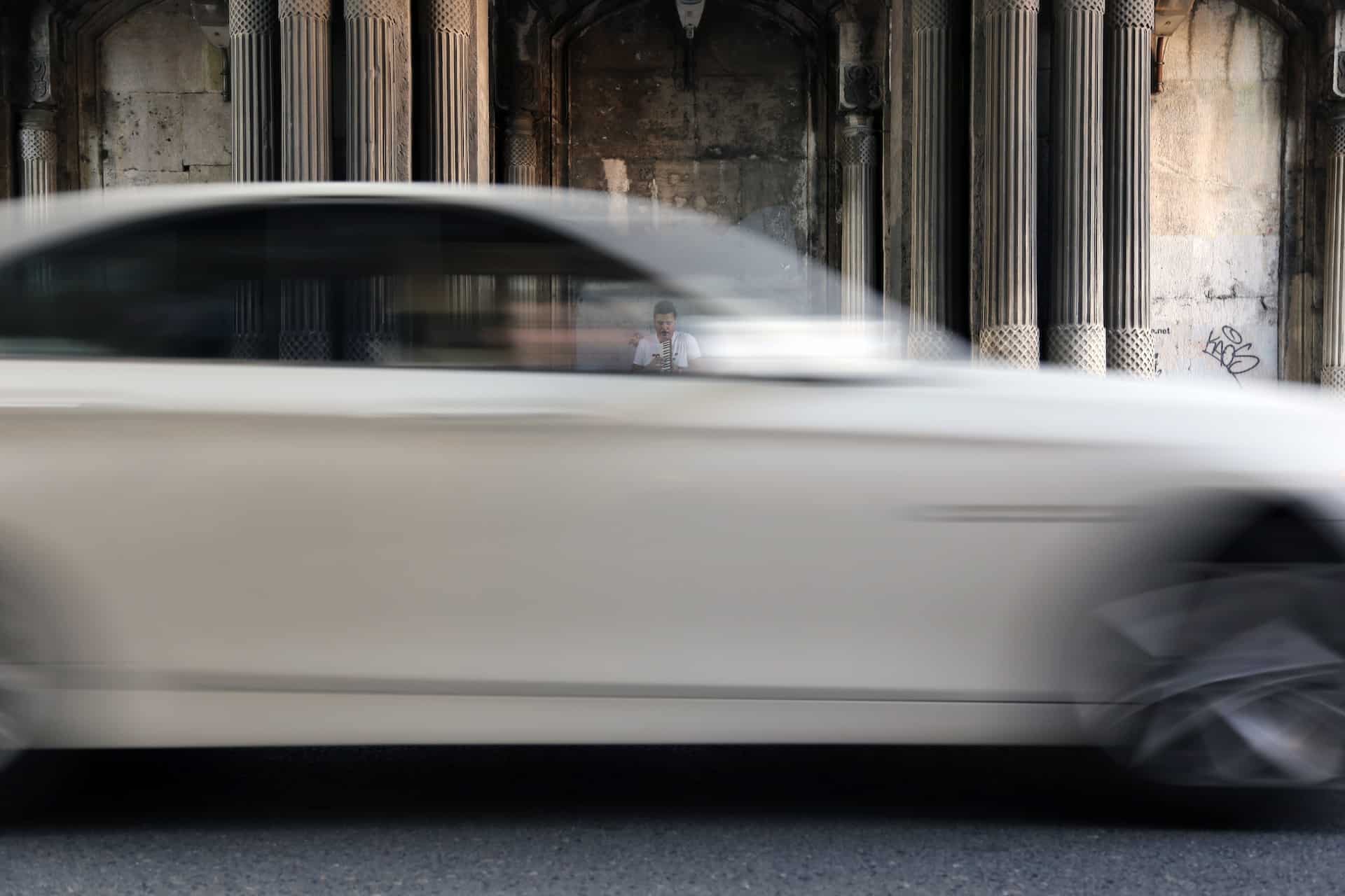 white car driving by historic building