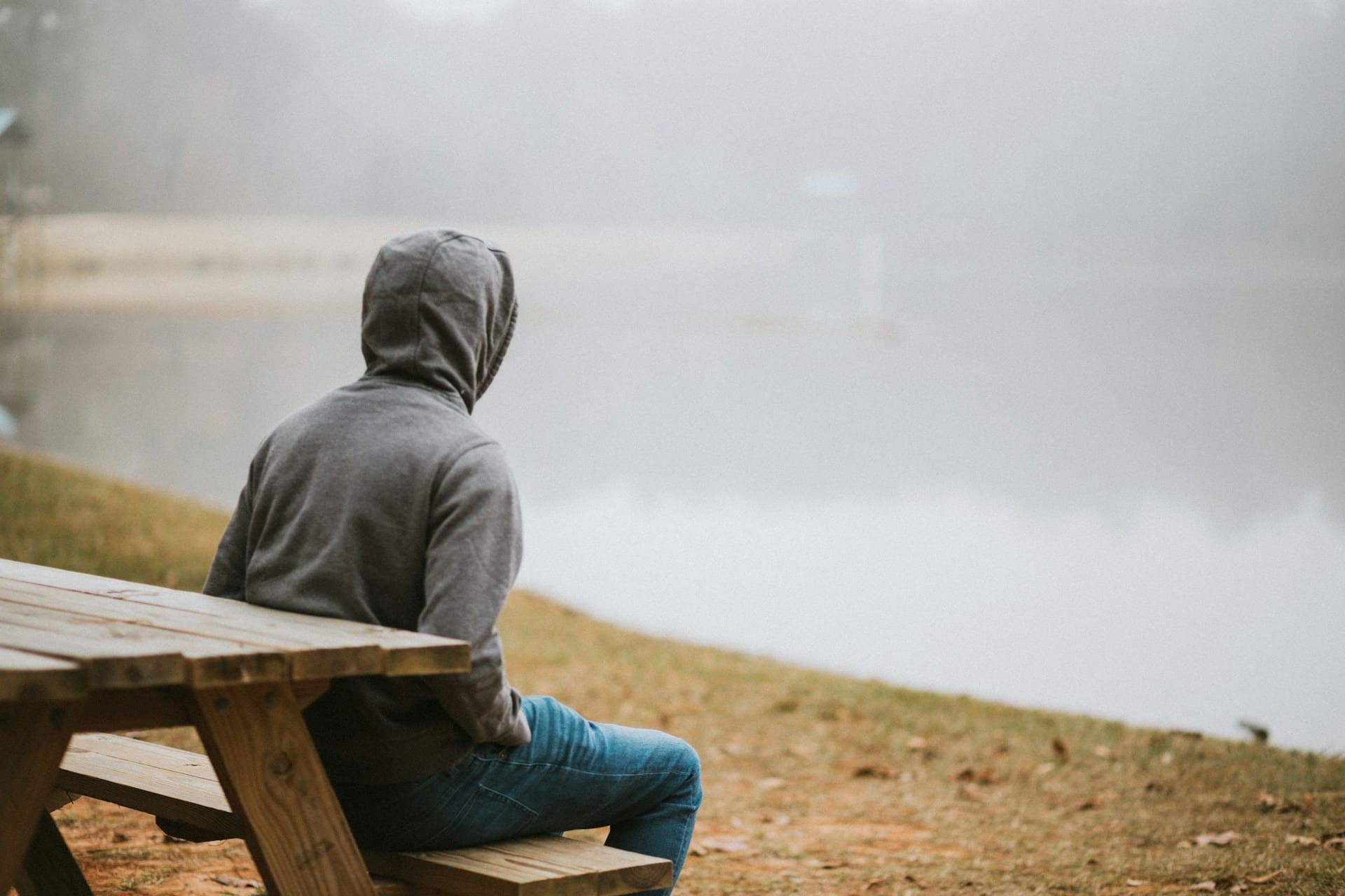 person sitting on bench by themselves by a lake